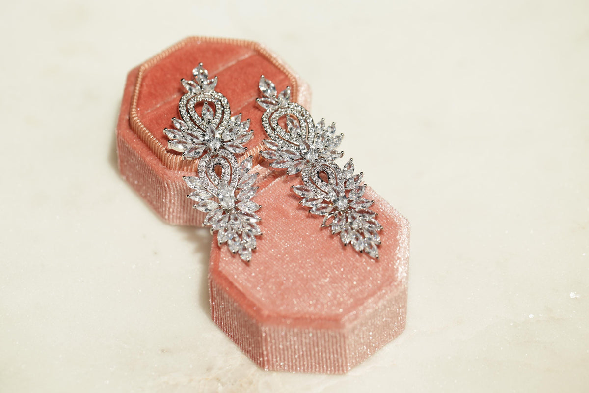A pair of elegant diamond earrings rests in a pink velvet jewelry box, showcasing their intricate designs and sparkling gemstones.