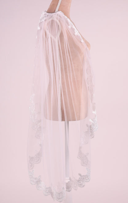A mannequin wearing a white lace veil with a delicate floral pattern.