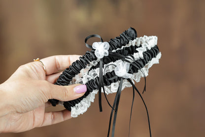 A hand holding a black and white garter with white lace trim.