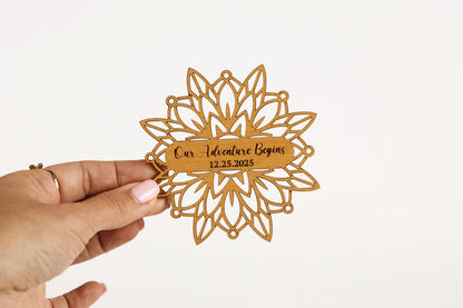 A hand holding a wooden ornament with a floral design and text on it.