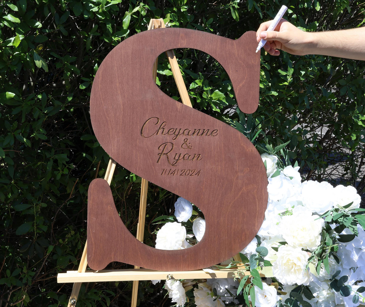 a person writing on a wooden sign with flowers in the background