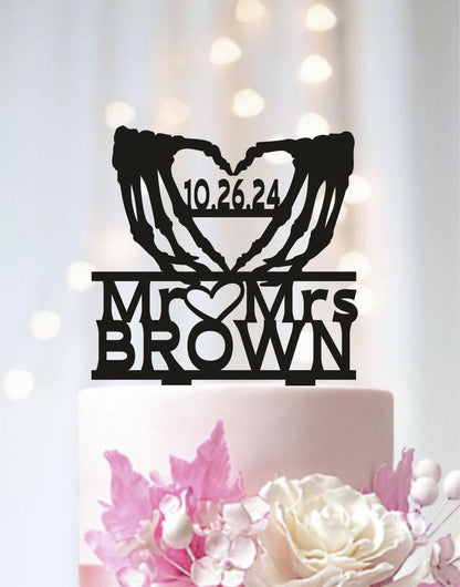 A black silhouette of a heart with the text "10.26.24" and "MR & MRS BROWN" written on it, placed on top of a white cake.