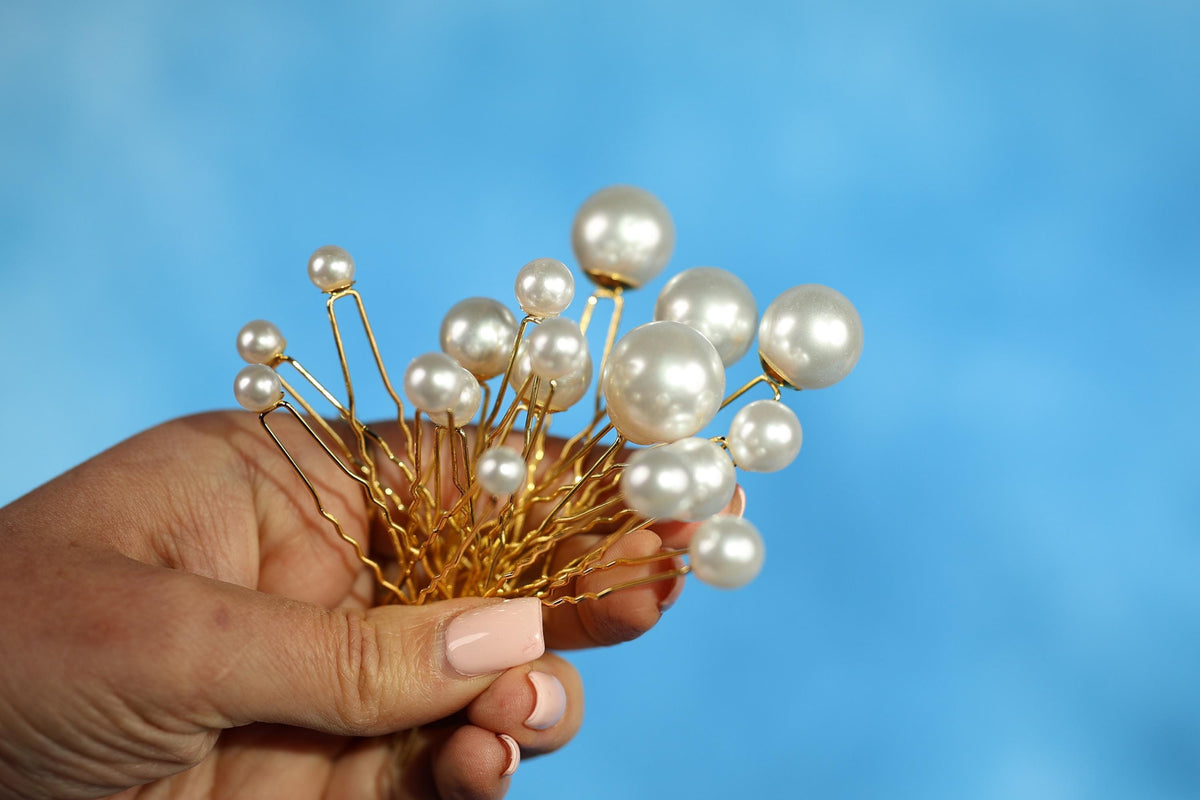 A hand holding a cluster of gold-colored metal pins with white pearls attached to them against a blue background.