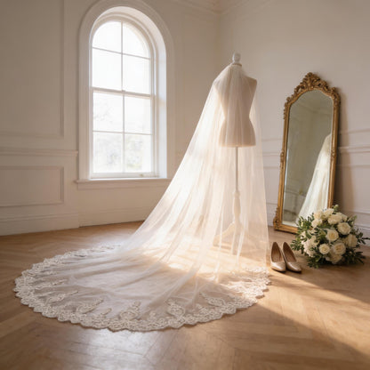 a white wedding dress with a long, flowing veil, placed on a mannequin in a room with a large window and a mirror.