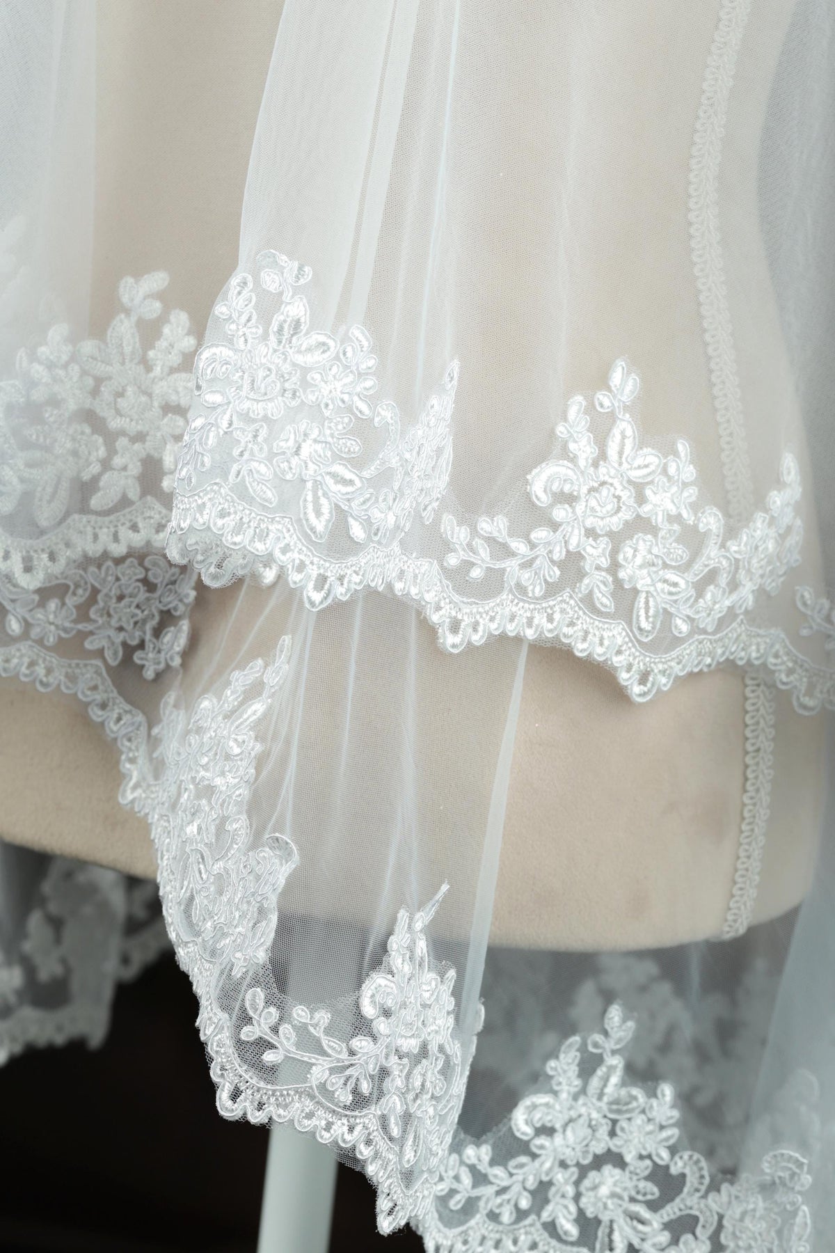 A close-up view of a delicate, white lace veil with intricate floral embroidery.