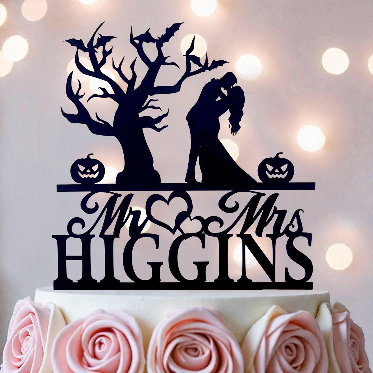 A black silhouette of a couple embracing, with a tree and pumpkins as decorative elements, is displayed on top of a white cake.