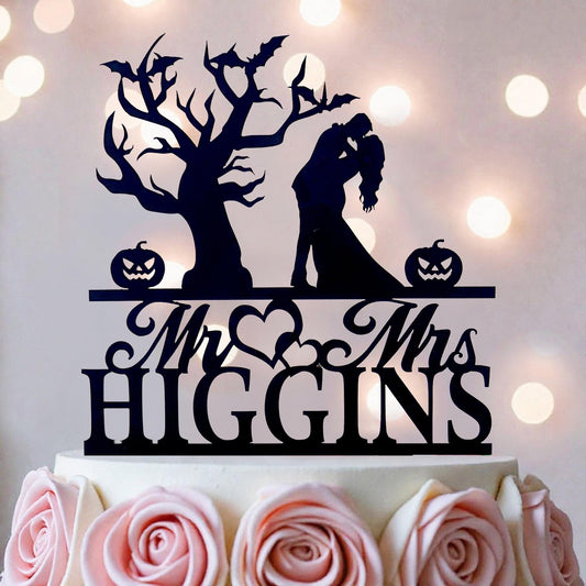 A black silhouette of a couple embracing, with a tree and pumpkins as decorative elements, is displayed on top of a white cake.