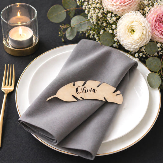 a table setting with a white plate, a gray napkin, a wooden place card, a candle, and some flowers.