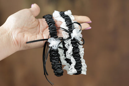 A hand holding a pair of black and white lace garter bands with white flowers.