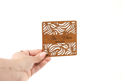 A hand holding a wooden coaster with a decorative design.