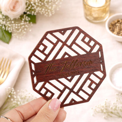 A hand holding a wooden coaster with a geometric pattern and text engraved on it.