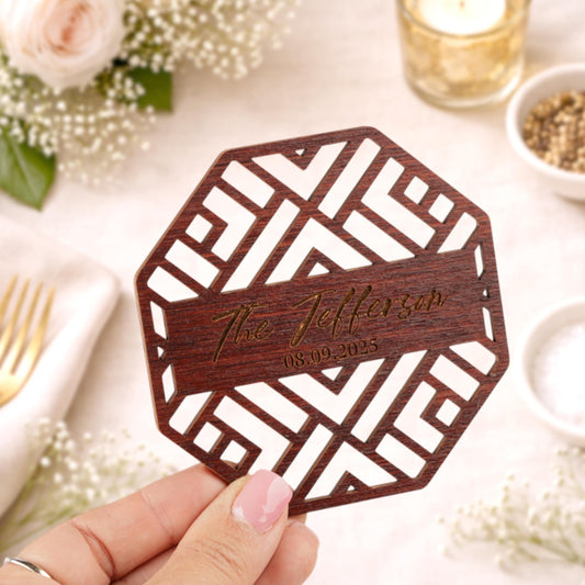 A hand holding a wooden coaster with a geometric pattern and text engraved on it.