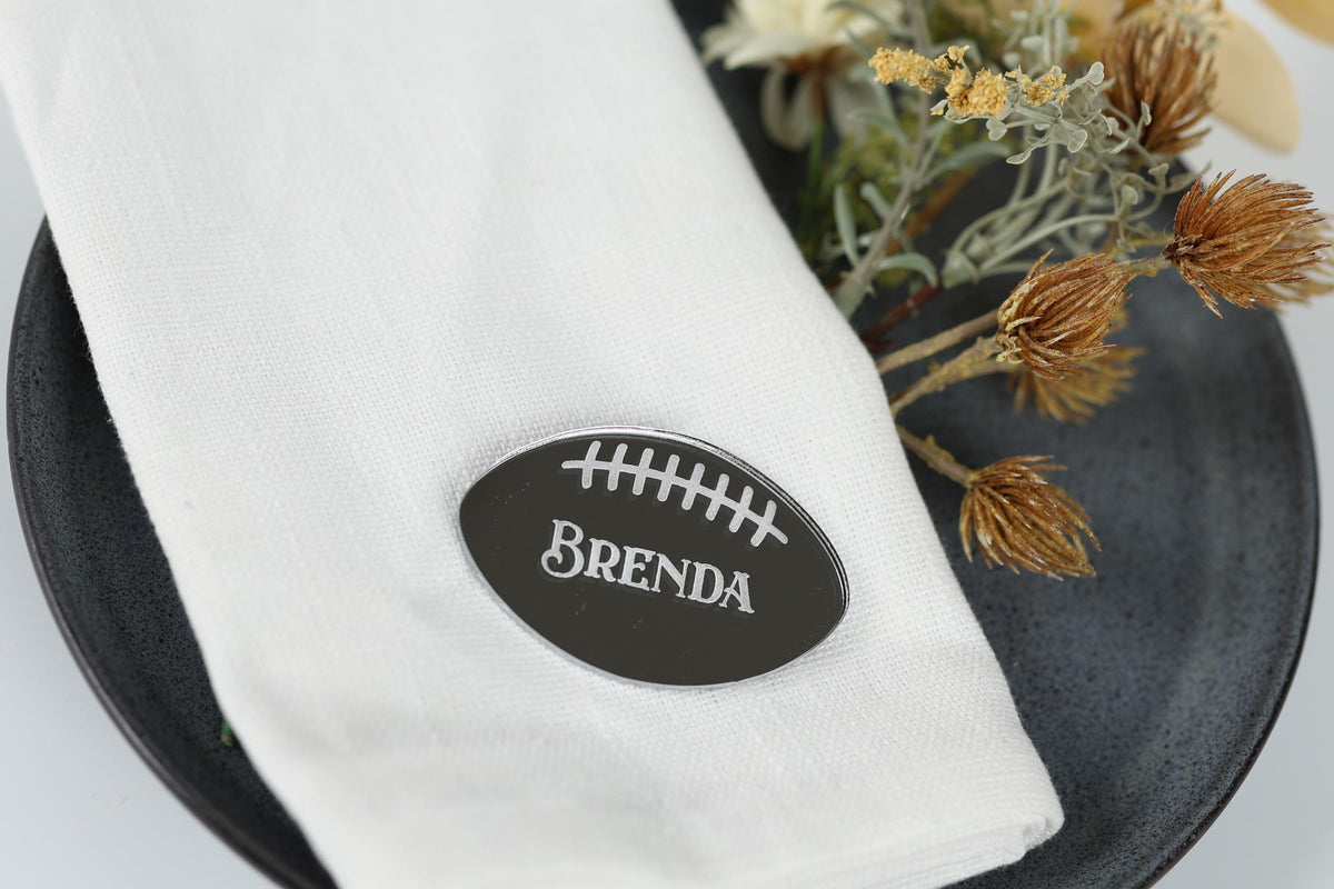 A white napkin with a black oval-shaped name tag that says "BENDA" on it, placed on a black plate with some dried flowers.