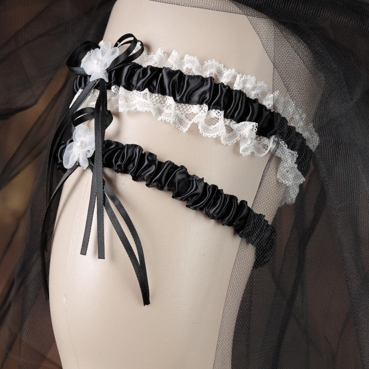 A mannequin wearing a black and white lace garter belt with a black ribbon and white flowers.
