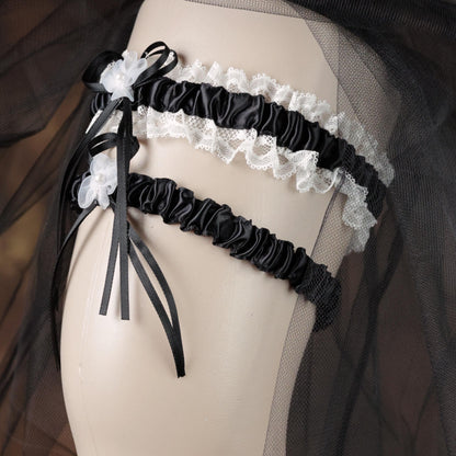 A mannequin wearing a black and white lace garter belt with a black ribbon and white flowers.