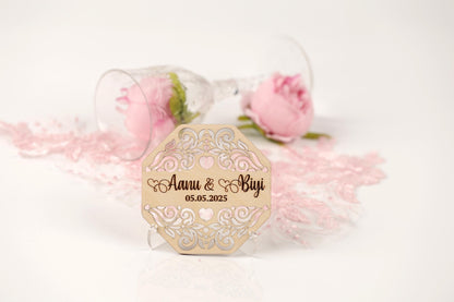 a wooden wedding card with a floral design, placed on a white surface next to a glass of wine and a pink rose.
