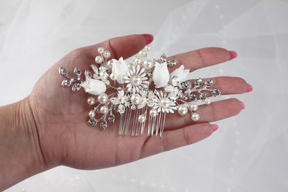 A hand holding a decorative hair accessory with white flowers and pearls.