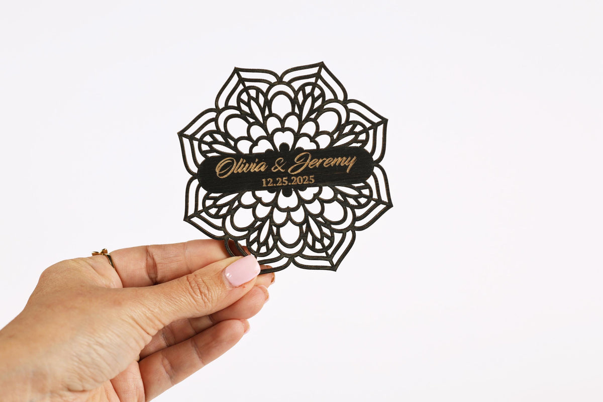 A hand holding a decorative paper cutout with the names 'Olivia & Jeremy' and the date '12.25.2025' printed on it.