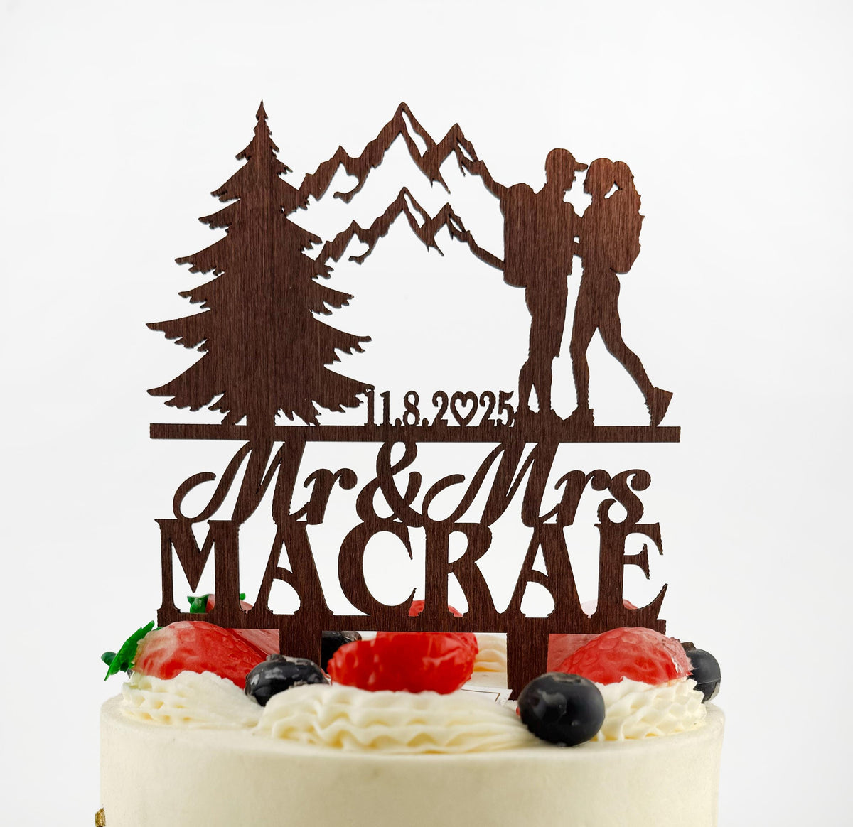 A wooden cake topper with a silhouette of a couple and mountains, along with the names 'Mr & Mrs' and the date '11.8.29'.