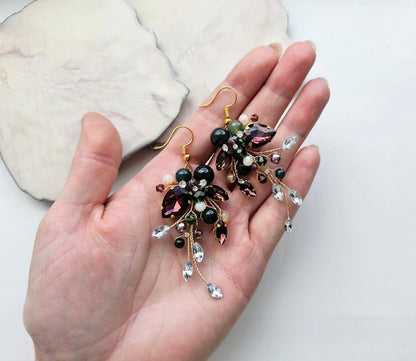 A hand holding a pair of earrings with colorful beads and dangling charms.