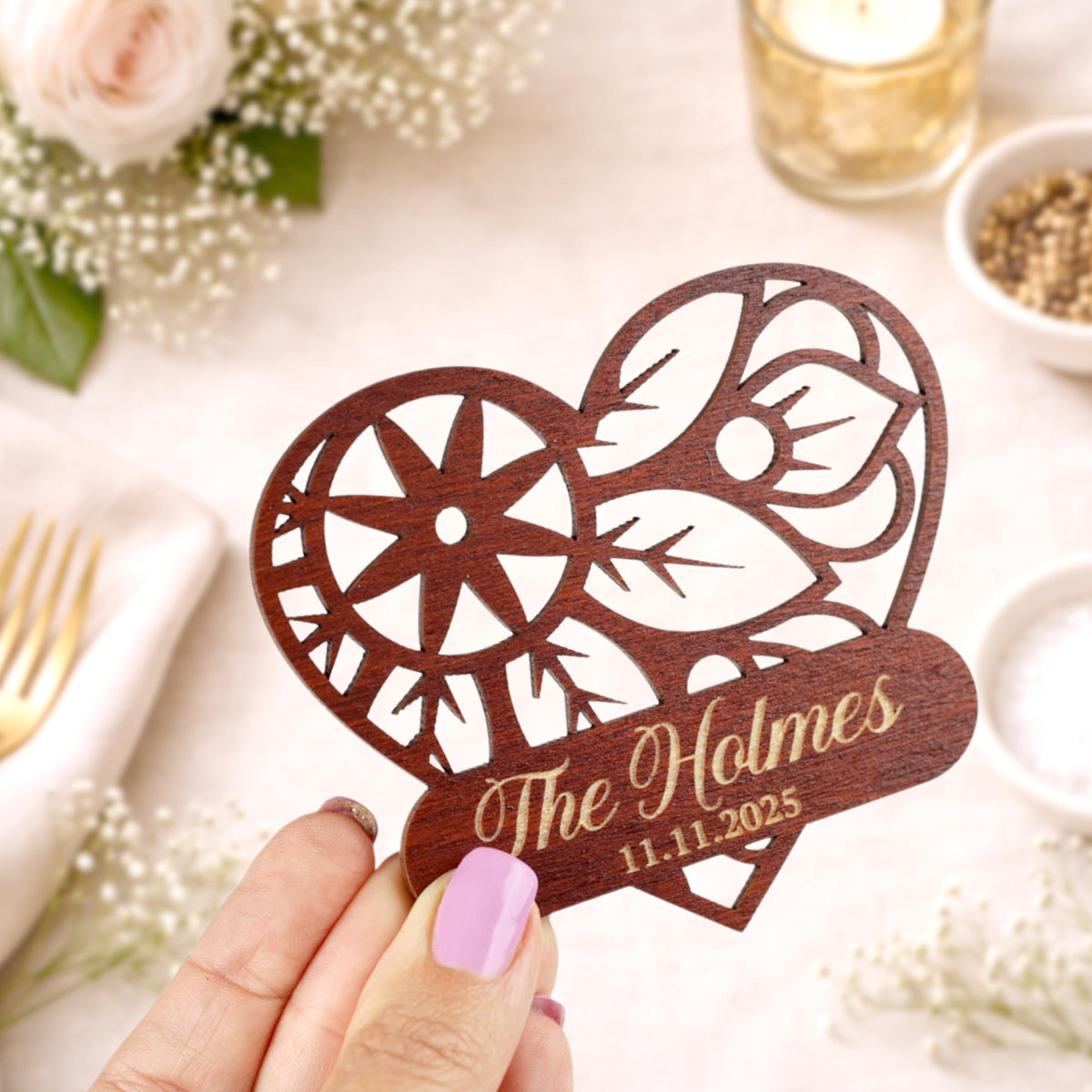 A wooden heart-shaped card with a floral design and the name "The Holmes" printed on it, held in a hand.