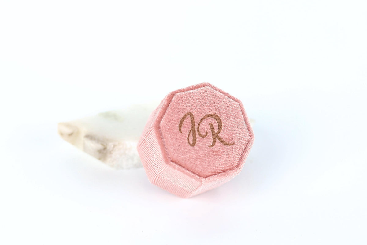 A pink, hexagonal jewelry box with the initials "JR" printed on it, placed on a white background.