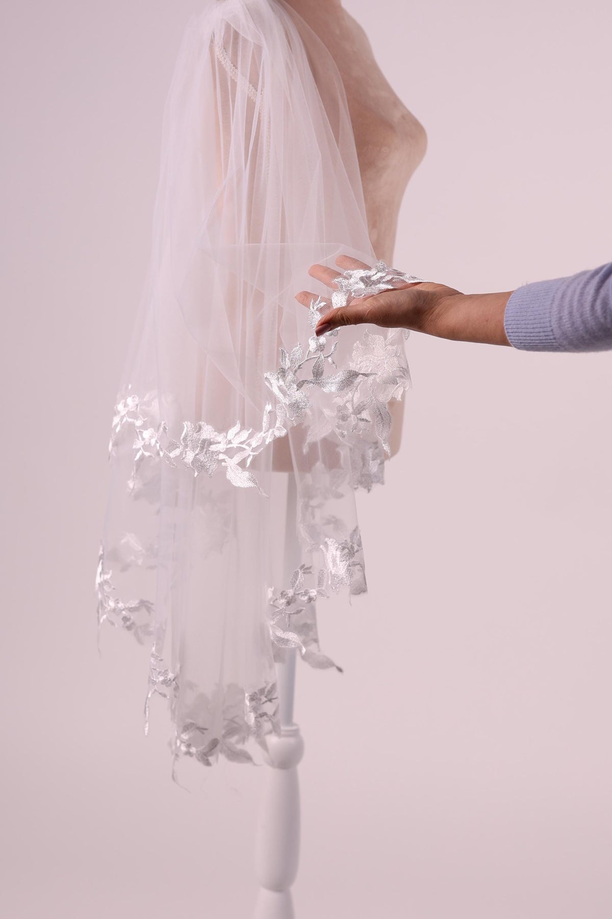 A hand holding a white veil with silver floral decorations.