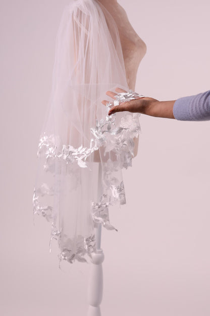 A hand holding a white veil with silver floral decorations.