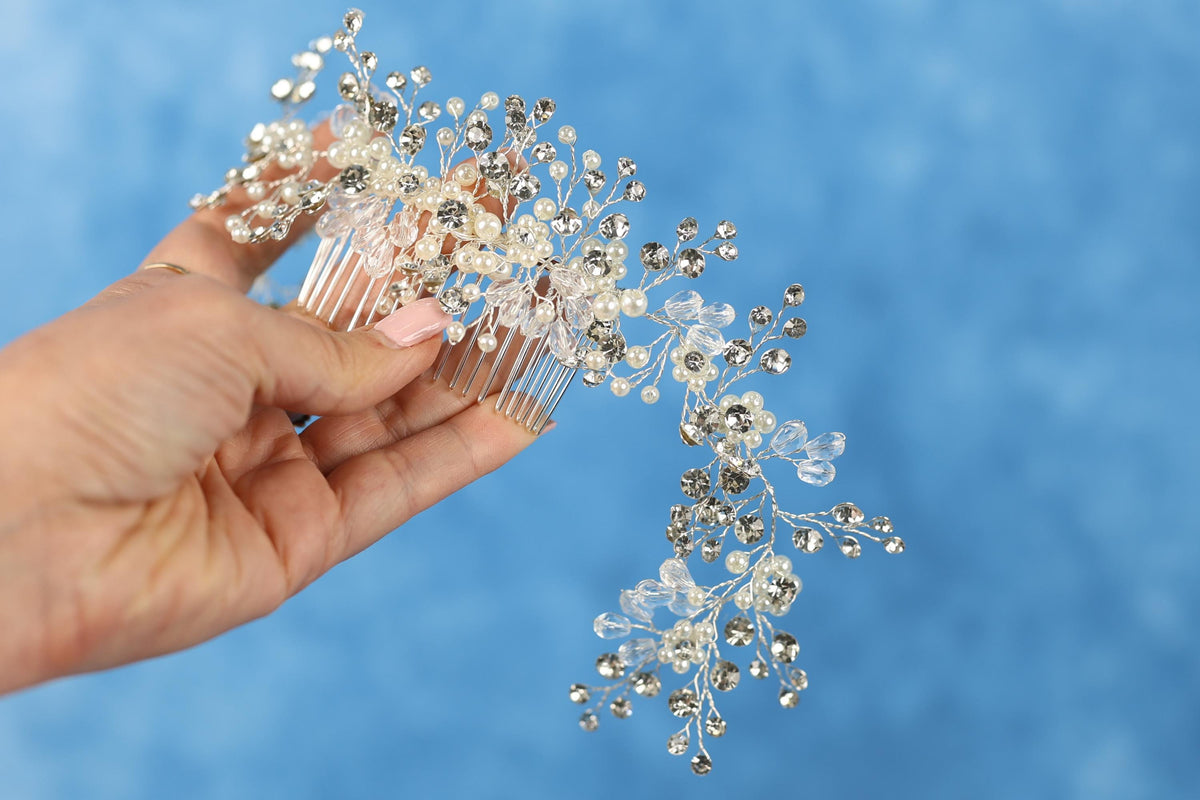 A hand holding a decorative hair accessory with a floral or leaf-like design, against a blue background.