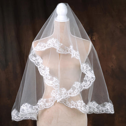 A mannequin wearing a white lace veil with intricate floral embroidery.