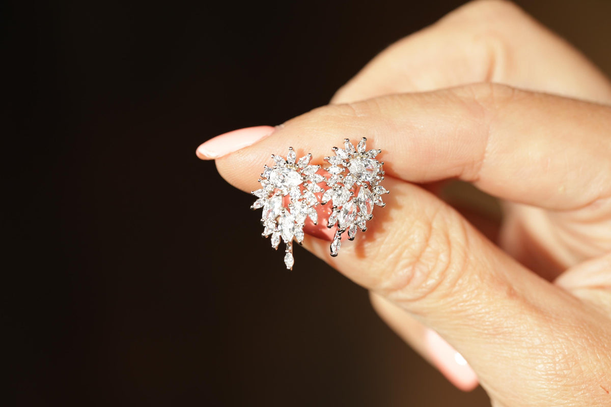 A close-up image of a person's hand holding a pair of diamond earrings.