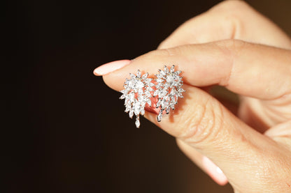 A close-up image of a person's hand holding a pair of diamond earrings.