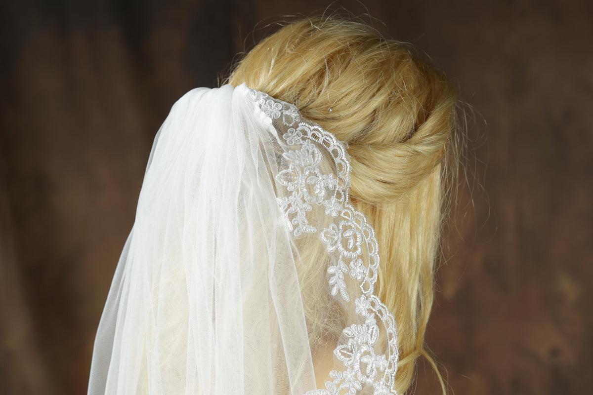 A close-up view of a woman's blonde hair, with a white veil adorned with lace trim, partially obscuring her face.