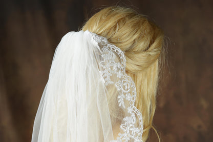 A close-up view of a woman's blonde hair, with a white veil adorned with lace trim, partially obscuring her face.