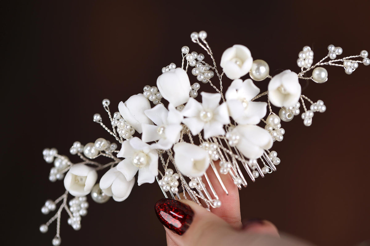 a close up of a person's hand holding a white flower and pearl hair