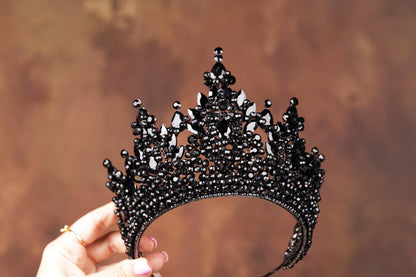 a hand holding a black tiara against a brown background