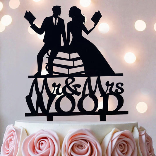 A silhouette of a man and a woman holding books, with the text "Mr & Mrs Wood" below them, on a cake topper.