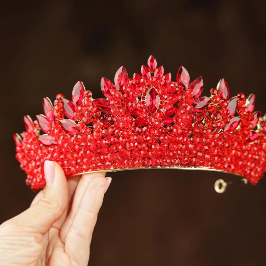 A hand is holding a red, ornate tiara adorned with numerous red gemstones.
