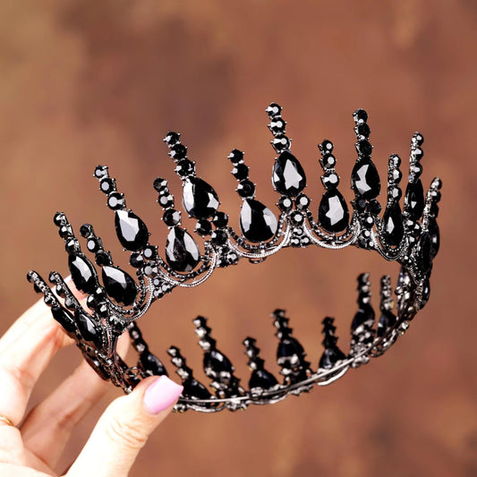 A hand holding a black ornate crown adorned with black gemstones against a brown background.