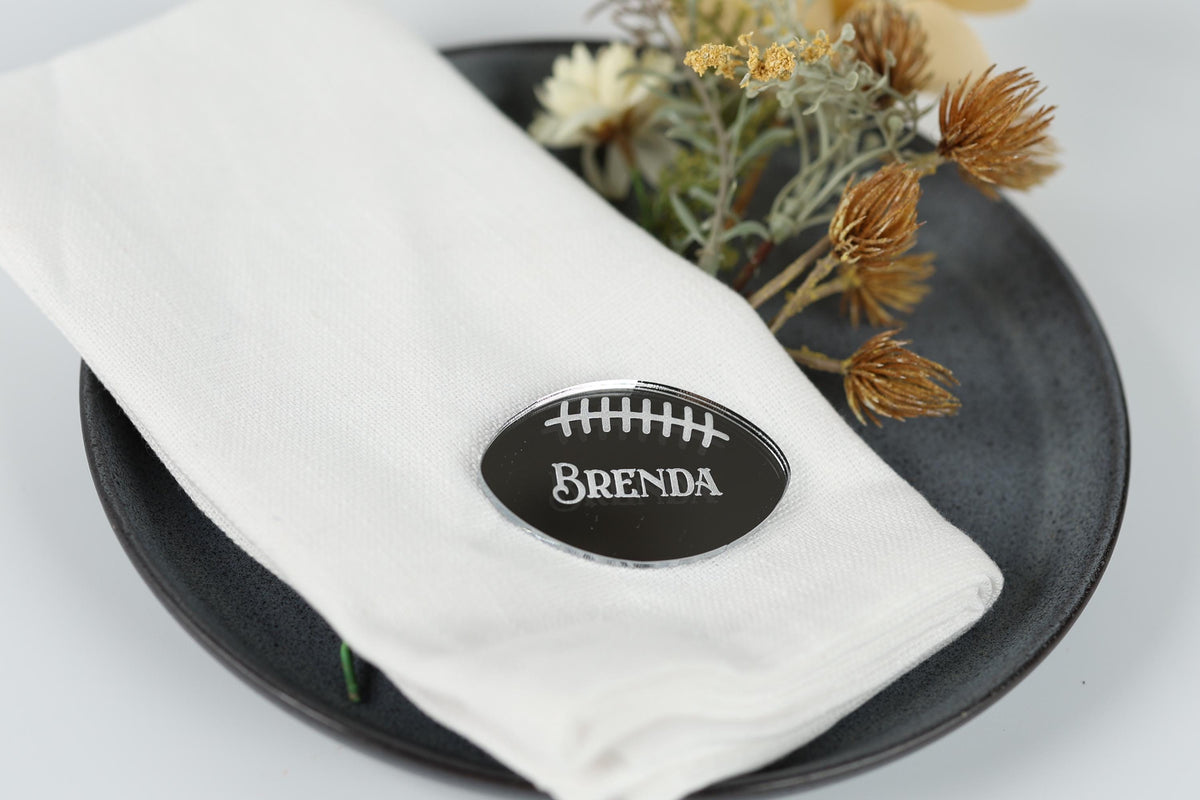 A white napkin with a black name tag that says "BENDA" placed on a black plate, with some dried flowers and a small green plant in the background.