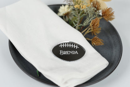 A white napkin with a black name tag that says "BENDA" placed on a black plate, with some dried flowers and a small green plant in the background.
