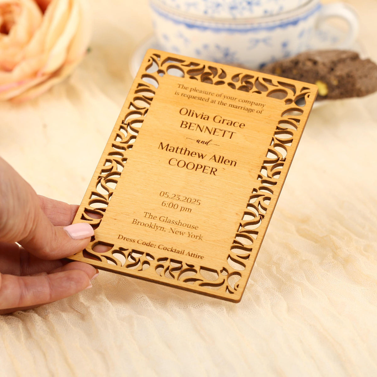 A hand holding a wooden wedding invitation card with a decorative frame.