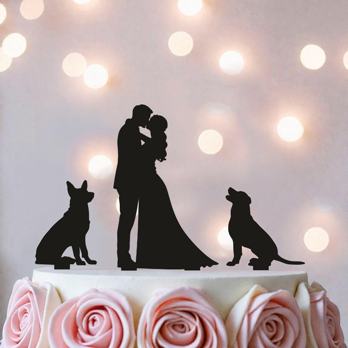 A silhouette of a couple embracing a dog on a cake topper, with pink roses on the cake.