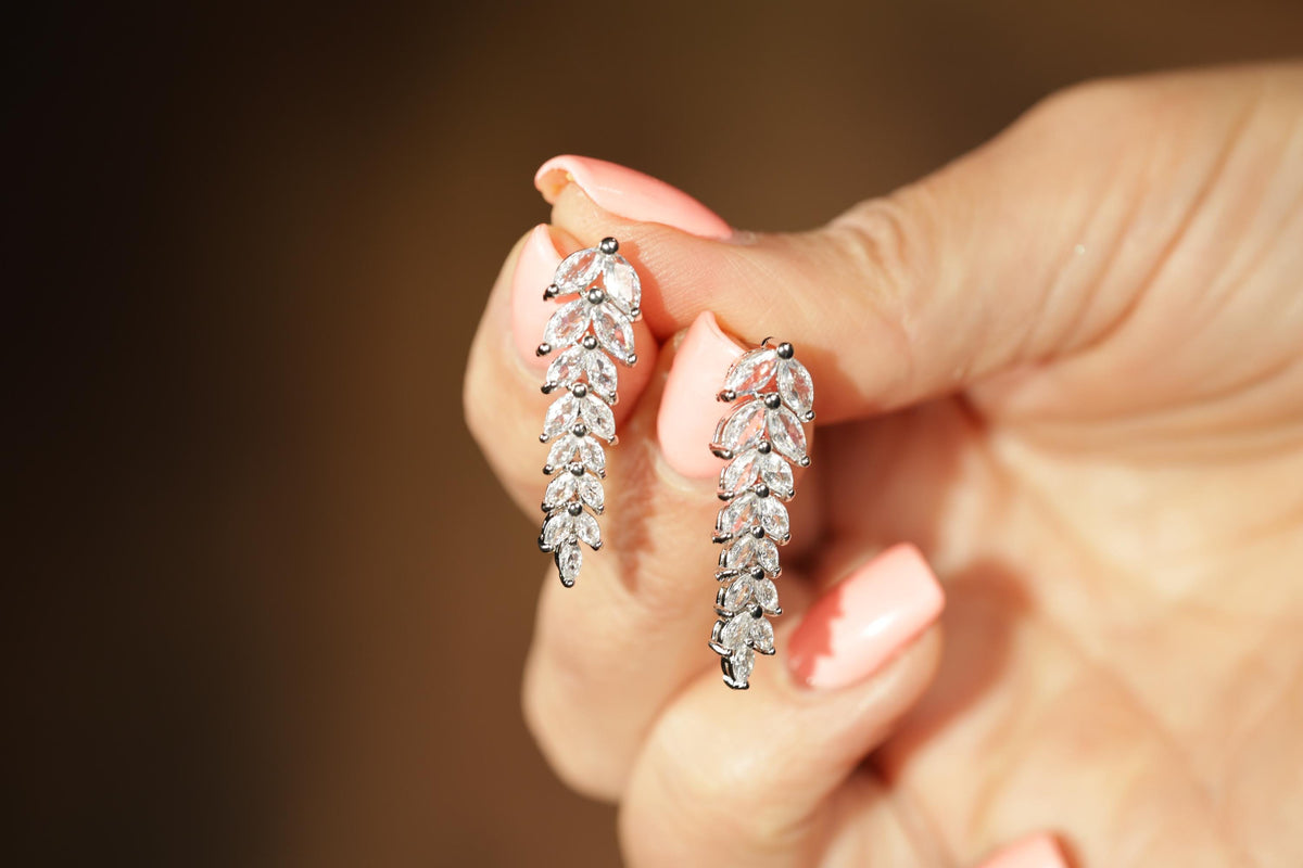 A close-up of a person's hand holding a pair of diamond earrings.