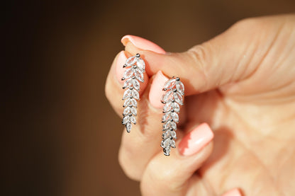 A close-up of a person's hand holding a pair of diamond earrings.