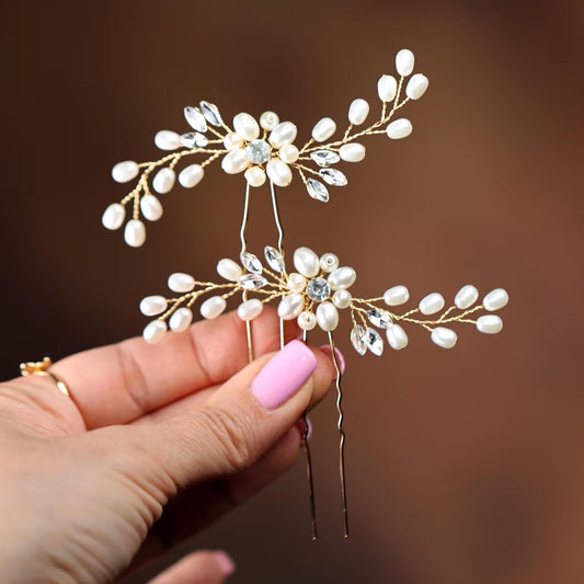 A hand holding a pair of decorative hair clips with white pearls and clear gemstones.