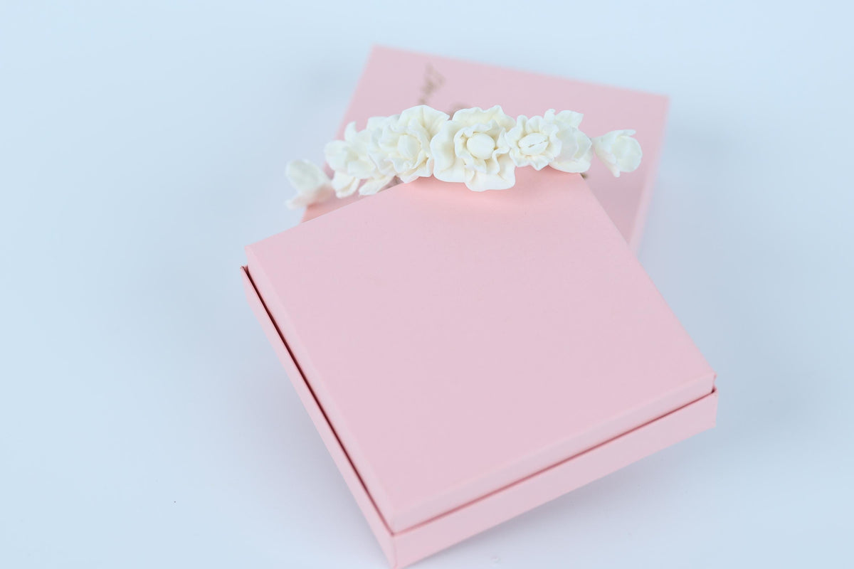 A pink gift box with a white floral decoration on top, placed on a white background.