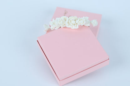 A pink gift box with a white floral decoration on top, placed on a white background.