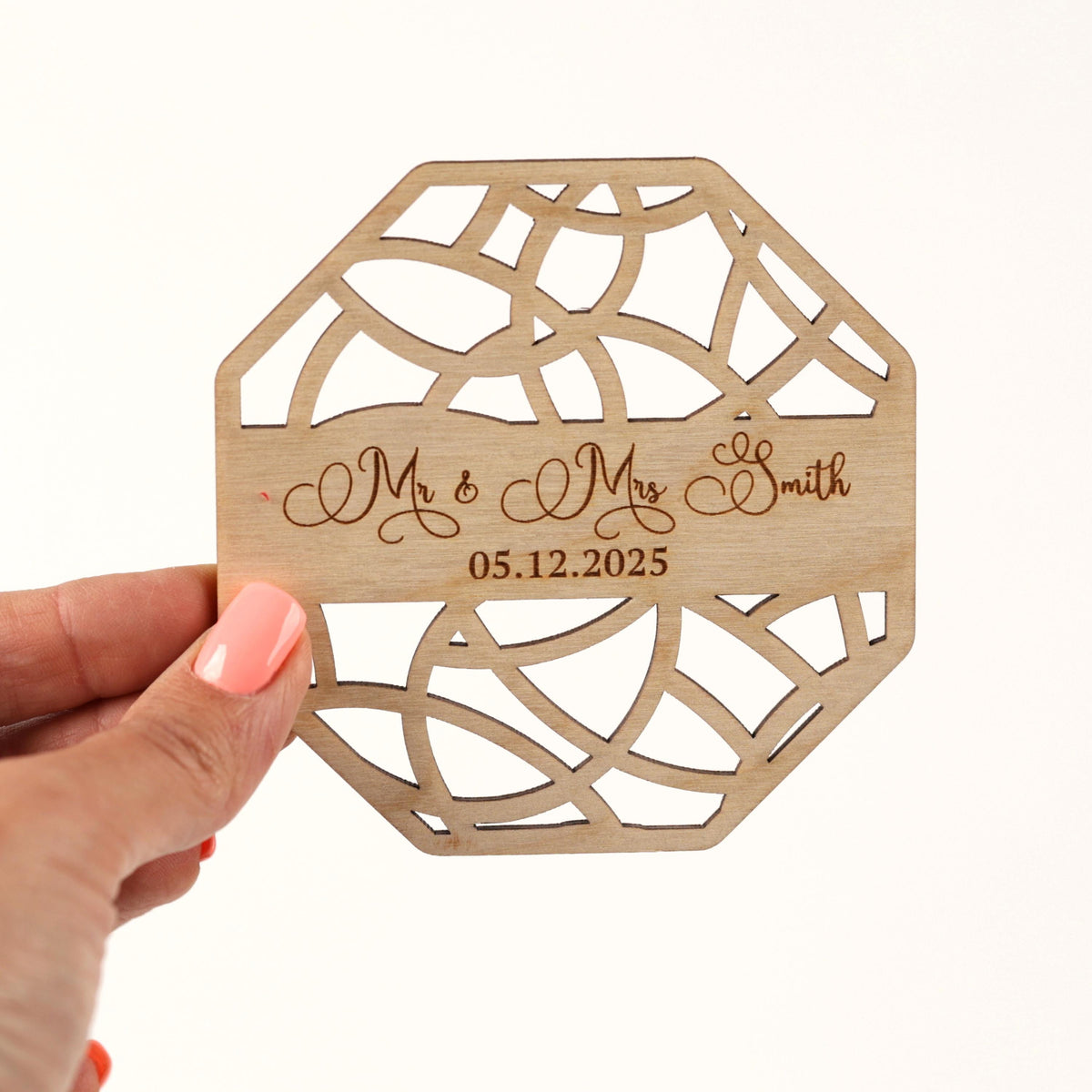 A hand holding a wooden coaster with the names 'Mr & Mrs Smith' and the date '05.12.2025' engraved on it.
