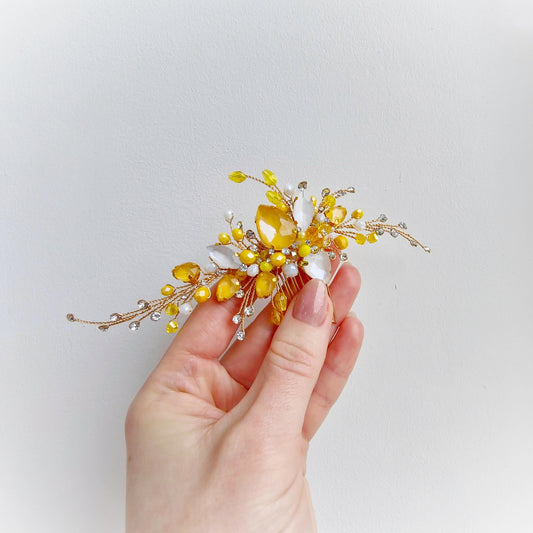 A hand holding a decorative hair accessory with yellow and white elements.